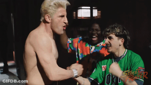 A Shirtless Man In A Street Fighter Shirt Holds Hands With Another Shirtless Man GIF
