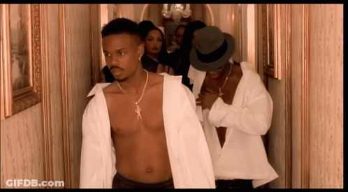 A Shirtless Man In A White Shirt Is Walking Down A Hallway With Other Men GIF