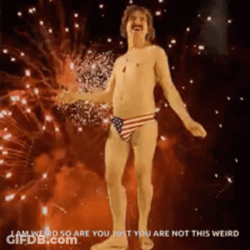 A Shirtless Man In An American Flag Underwear Is Dancing In Front Of Fireworks . GIF