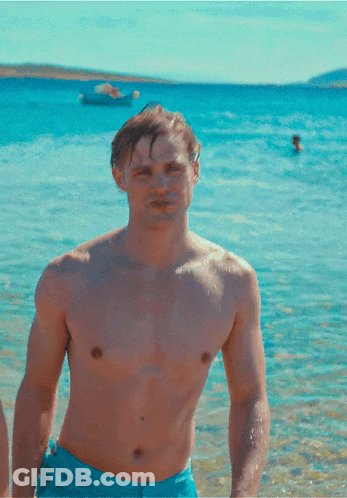 A Shirtless Man In Blue Shorts Stands On A Beach GIF