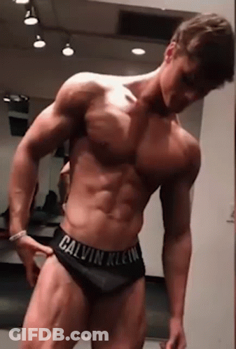 A Shirtless Man In Calvin Klein Underwear Is Standing In Front Of A Mirror In A Gym . GIF