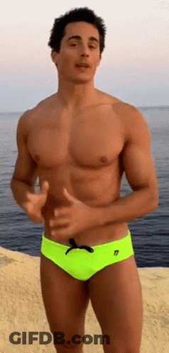 A Shirtless Man In Neon Yellow Swim Trunks Is Standing On The Beach Near The Ocean . GIF