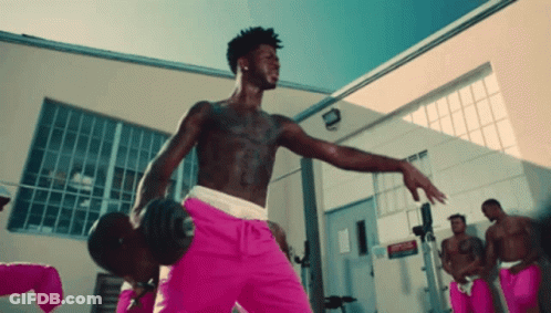 A Shirtless Man In Pink Shorts Is Holding A Dumbbell In A Gym GIF