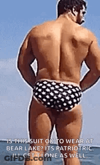 A Shirtless Man In Polka Dot Swim Trunks Is Standing On The Beach . GIF