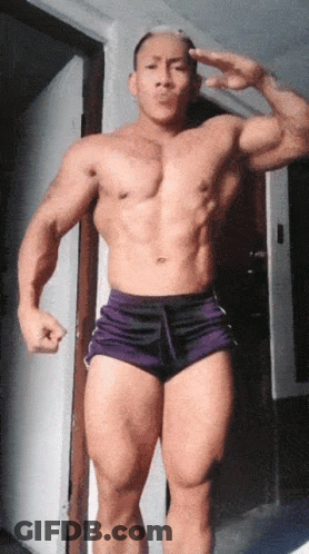 A Shirtless Man In Purple Shorts Is Giving The Peace Sign GIF