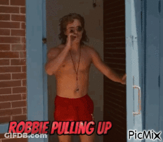A Shirtless Man In Red Shorts Is Standing In Front Of A Brick Wall With The Words Robbie Pulling Up On The Bottom GIF