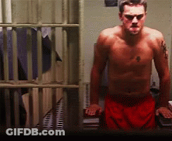 A Shirtless Man In Red Shorts Is Standing In Front Of A Jail Cell GIF