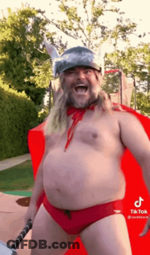 A Shirtless Man In Red Swim Trunks And A Viking Helmet Is Holding A Hammer And Smiling . GIF