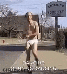 A Shirtless Man In Underwear Is Dancing On A Sidewalk In Front Of A Sign That Says Dancing Dancing . GIF