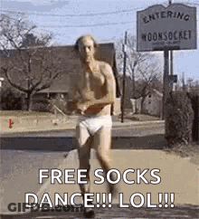A Shirtless Man In Underwear Is Running Down A Street In Front Of A Sign That Says Free Socks Dance LOL . GIF