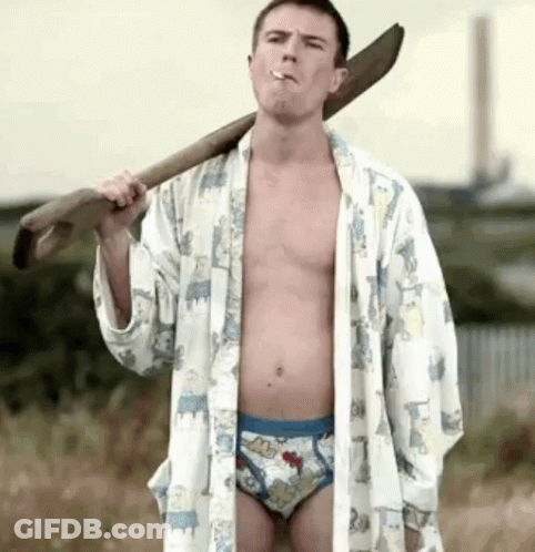A Shirtless Man In Underwear Is Smoking A Cigarette While Holding A Large Wooden Stick Over His Shoulder . GIF