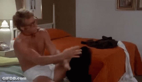 A Shirtless Man In White Underwear Is Sitting On A Bed In A Bedroom . GIF