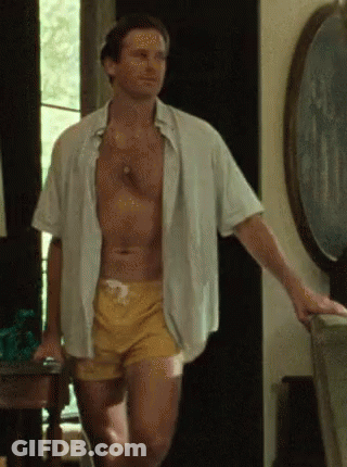 A Shirtless Man In Yellow Swim Trunks Is Standing In A Room . GIF