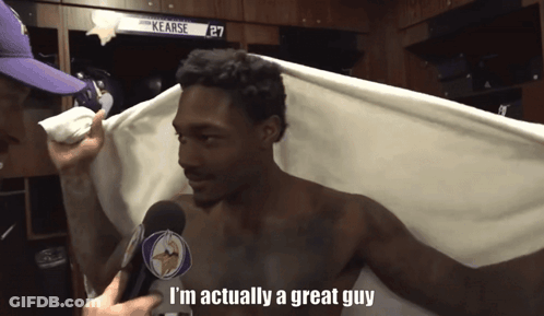 A Shirtless Man Is Being Interviewed In A Locker Room By A Man Wearing A Vikings Hat GIF