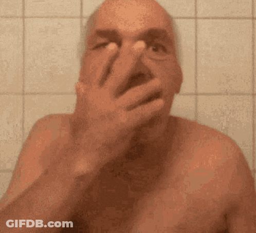 A Shirtless Man Is Covering His Face With His Hand In A Bathroom . GIF