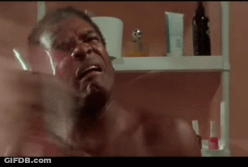 A Shirtless Man Is Crying In Front Of A Shelf With Bottles Of Perfume GIF