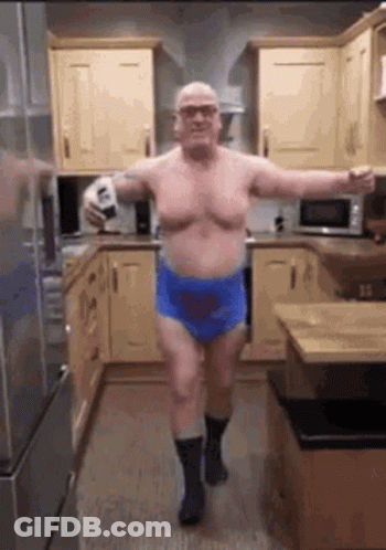 A Shirtless Man Is Dancing In A Kitchen While Holding A Bottle Of Beer . GIF