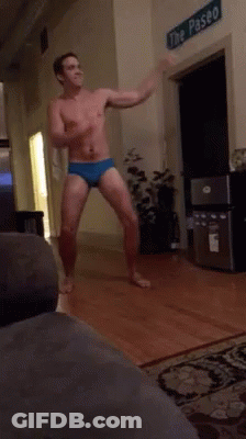 A Shirtless Man Is Dancing In A Living Room In Front Of A Sign That Says The Paseo GIF