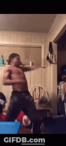 A Shirtless Man Is Dancing In A Living Room With A Chair In The Background GIF
