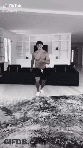 A Shirtless Man Is Dancing In A Living Room With A Couch . GIF