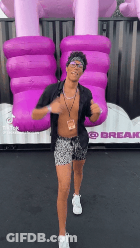 A Shirtless Man Is Dancing In Front Of A Giant Purple Inflatable Elephant GIF