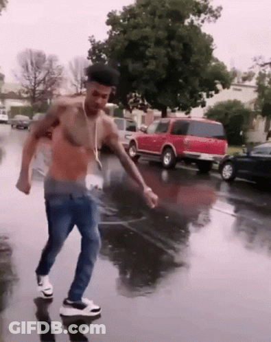 A Shirtless Man Is Dancing In The Rain On A Wet Street GIF