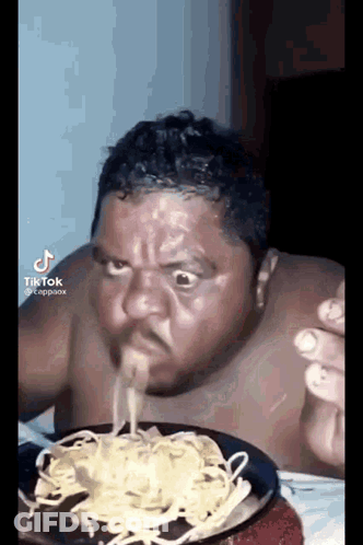 A Shirtless Man Is Eating A Plate Of Noodles With His Mouth Open . GIF