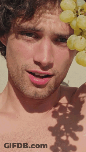 A Shirtless Man Is Holding A Bunch Of Grapes Over His Head GIF