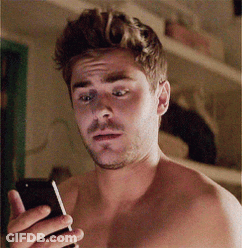 A Shirtless Man Is Holding A Cell Phone In His Hand GIF