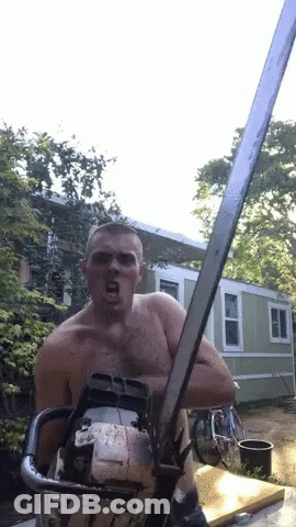 A Shirtless Man Is Holding A Chainsaw In Front Of A House GIF