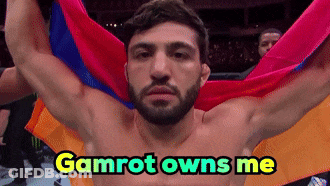 A Shirtless Man Is Holding A Colorful Flag With The Words Gamrot Owns Me Above Him GIF