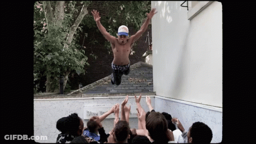 A Shirtless Man Is Jumping In The Air With His Arms Outstretched In Front Of A Crowd GIF