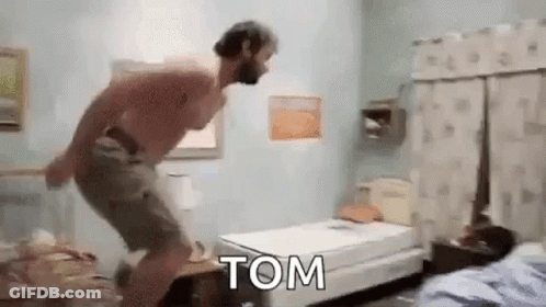A Shirtless Man Is Jumping On A Bed In A Bedroom With The Word Tom Written On It . GIF