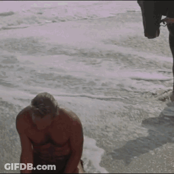 A Shirtless Man Is Kneeling On The Beach Near The Ocean GIF