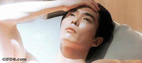 A Shirtless Man Is Laying In A Bathtub With His Hand On His Forehead GIF