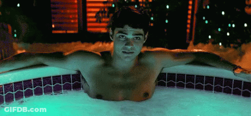 A Shirtless Man Is Laying In A Hot Tub Filled With Foam . GIF