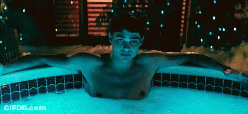 A Shirtless Man Is Laying In A Hot Tub With His Arms Outstretched At Night . GIF