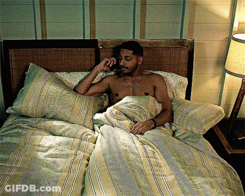 A Shirtless Man Is Laying In Bed Talking On A Phone GIF