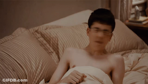 A Shirtless Man Is Laying In Bed With A Striped Comforter GIF