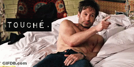 A Shirtless Man Is Laying On A Bed And Pointing At Himself With The Word Touche Above Him . GIF