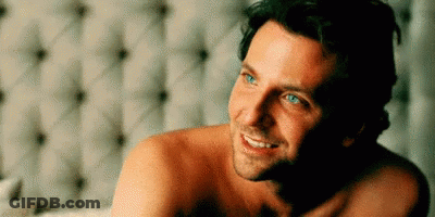 A Shirtless Man Is Laying On A Bed Smiling . GIF