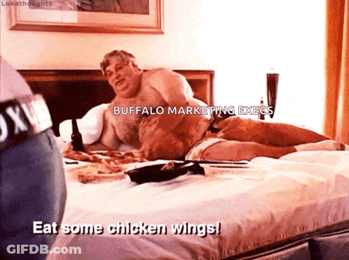 A Shirtless Man Is Laying On A Bed With The Words Eat Some Chicken Wings GIF