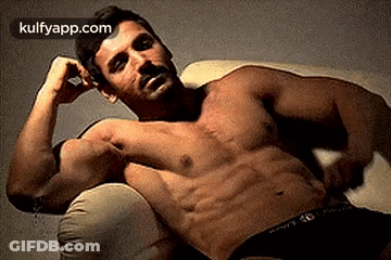 A Shirtless Man Is Laying On A Couch With His Hands On His Head . GIF