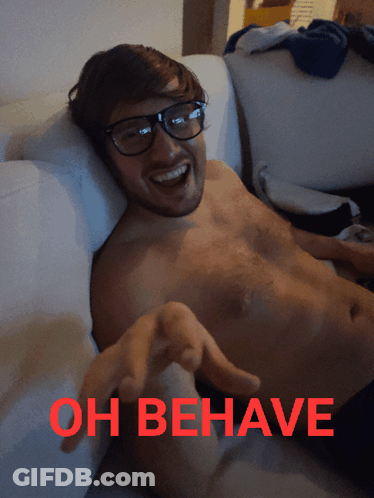 A Shirtless Man Is Laying On A Couch With The Words Oh Behave Written In Red GIF