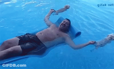 A Shirtless Man Is Laying On A Raft In A Swimming Pool With His Dog . GIF