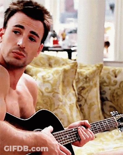 A Shirtless Man Is Playing An Acoustic Guitar On A Couch GIF