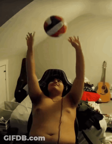 A Shirtless Man Is Playing With A Volleyball In A Bedroom GIF