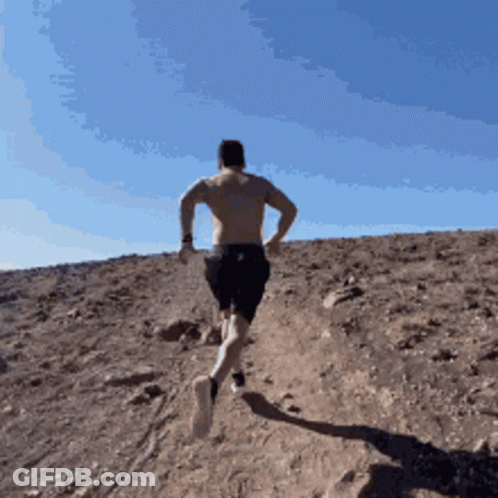 A Shirtless Man Is Running Up A Hill In The Desert GIF