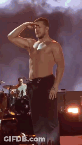 A Shirtless Man Is Saluting On A Stage In Front Of A Drummer . GIF