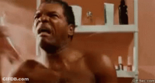 A Shirtless Man Is Shaving His Face In Front Of A Mirror In A Bathroom . GIF